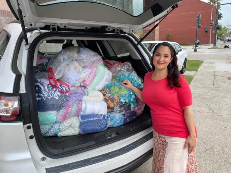 Melanie standing beside a car boot packed full of bagged handmade blankets ready for delivery