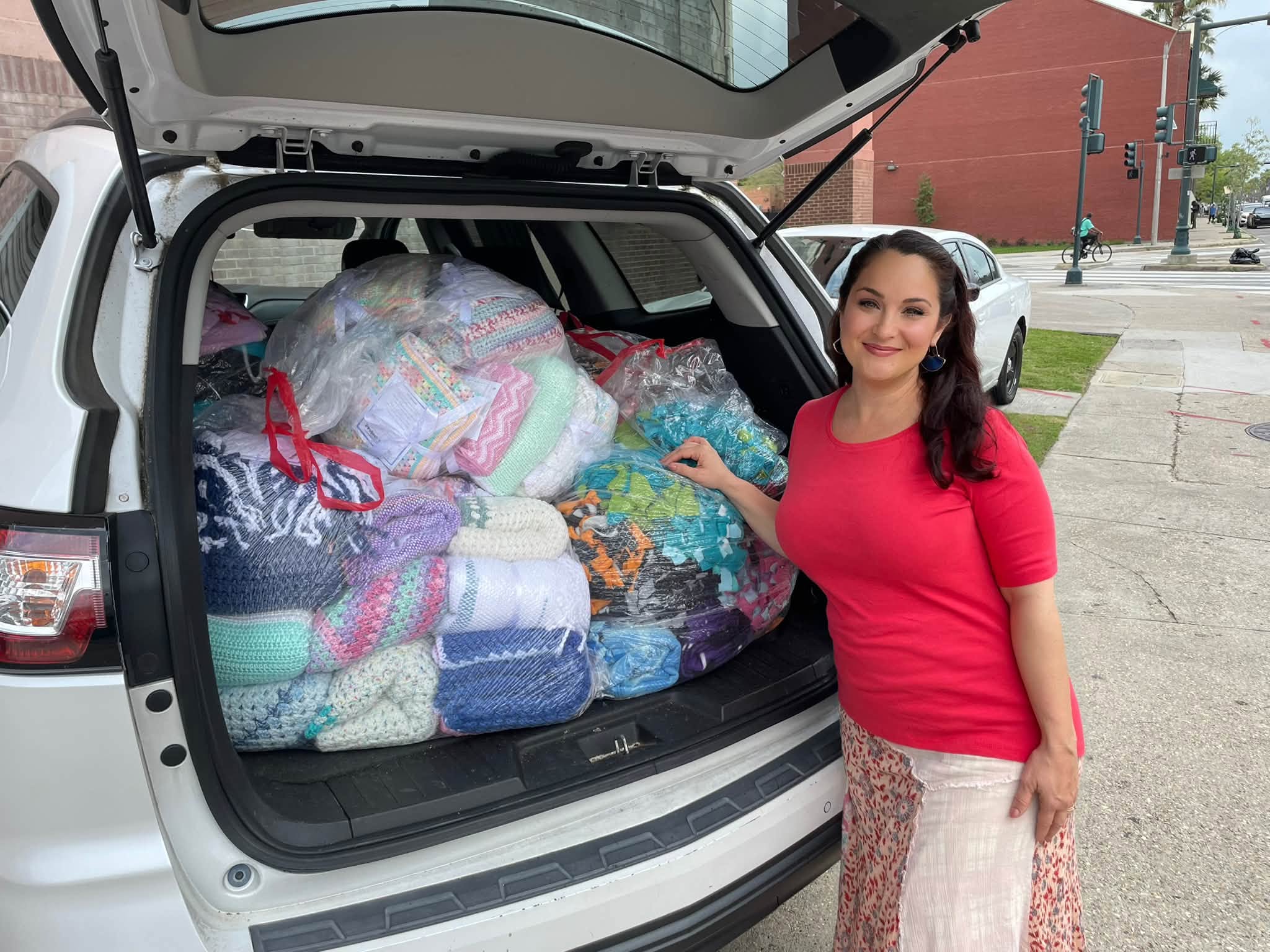 Melanie standing beside a car boot packed full of bagged handmade blankets ready for delivery
